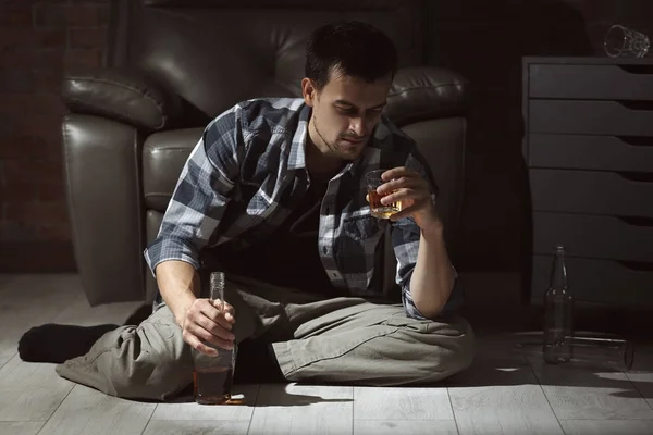 Ο άνθρωπος που κάθεται στο πάτωμα στο σπίτι και πίνοντας ουίσκι. Ο αλκοολισμός έννοια — Φωτογραφία Αρχείου
