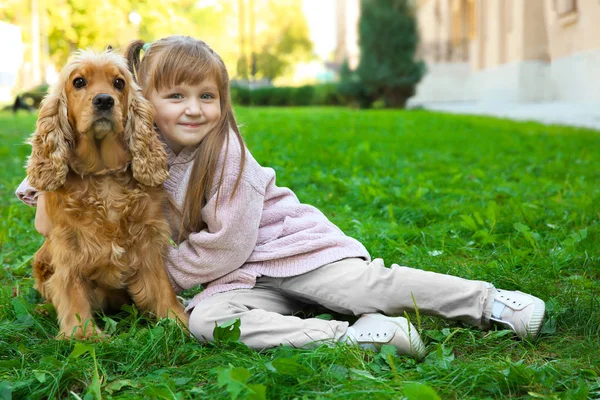 Nettes kleines Mädchen mit lustigem Hund auf grünem Gras — Stockfoto