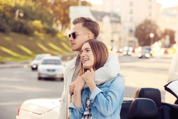 Feliz jovem casal de pé perto de carro moderno ao ar livre — Fotografia de Stock