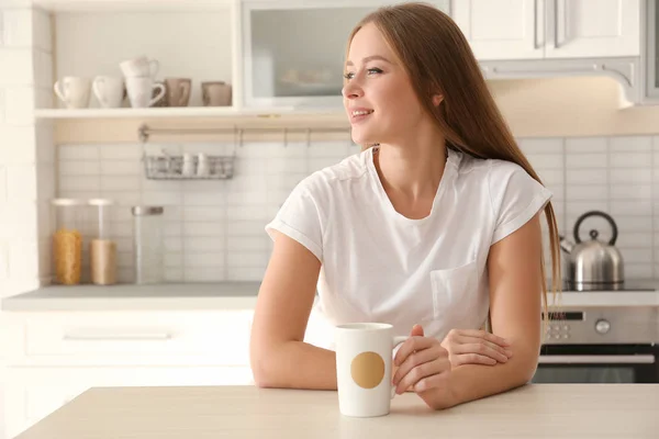 Beautiful young smiling woman with coffee at table on kitchen — Stock Photo, Image