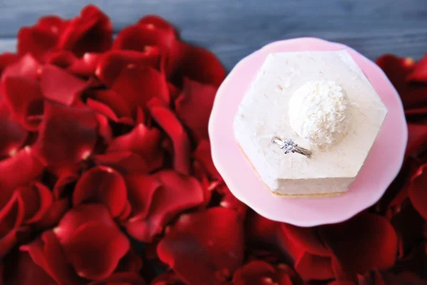 Stand com delicioso bolo, anel de noivado e pétalas na mesa — Fotografia de Stock