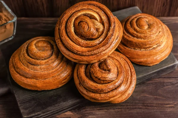 Placa de madeira com saborosos pães de canela na mesa — Fotografia de Stock
