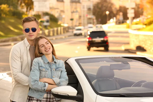 Feliz jovem casal de pé perto de carro moderno ao ar livre — Fotografia de Stock