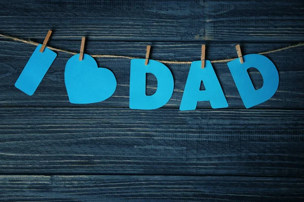 Phrase "I love dad" made of paper letters as greeting for Father's day on string against wooden background — Stock Photo, Image