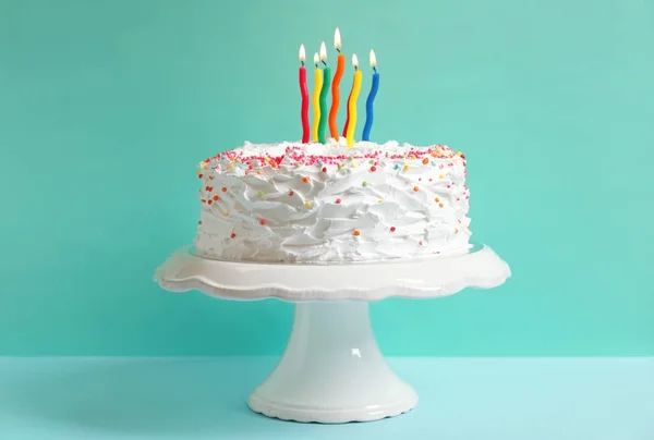 Soporte con pastel de cumpleaños y velas en la mesa contra la pared de color —  Fotos de Stock