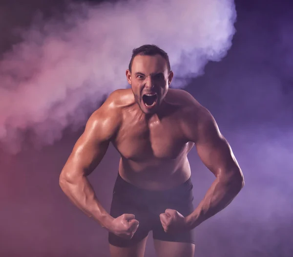 Muscular young bodybuilder in colorful smoke