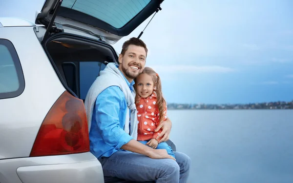 Unga far med flickan sitter i bilen stammen nära floden — Stockfoto