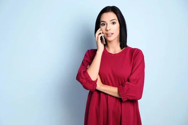 Mooie jonge vrouw spreken via de mobiele telefoon op kleur achtergrond — Stockfoto
