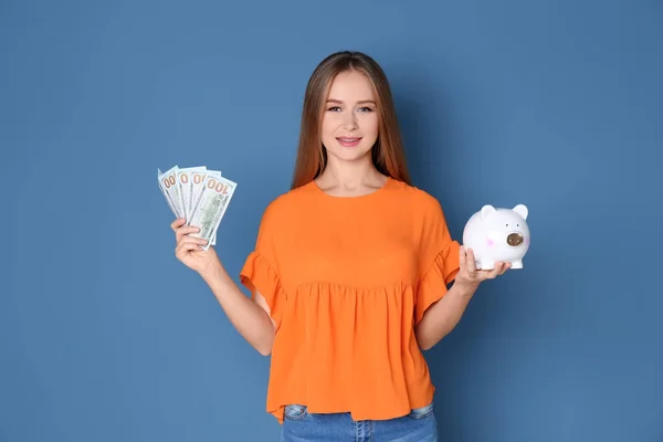 Młoda kobieta trzyma skarbonkę i pieniądze na kolor tła — Zdjęcie stockowe