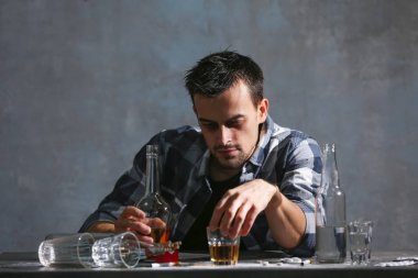 Alkol ve uyuşturucu ile masada oturan sarhoş adam. Alkolizm kavramı