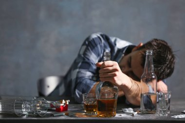 Alkol ve uyuşturucu ile masada oturan sarhoş adam. Alkolizm kavramı