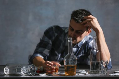 Alkol ve uyuşturucu ile masada oturan sarhoş adam. Alkolizm kavramı