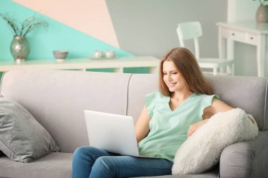 Evde koltukta istirahat ederken dizüstü bilgisayar kullanan güzel kadın