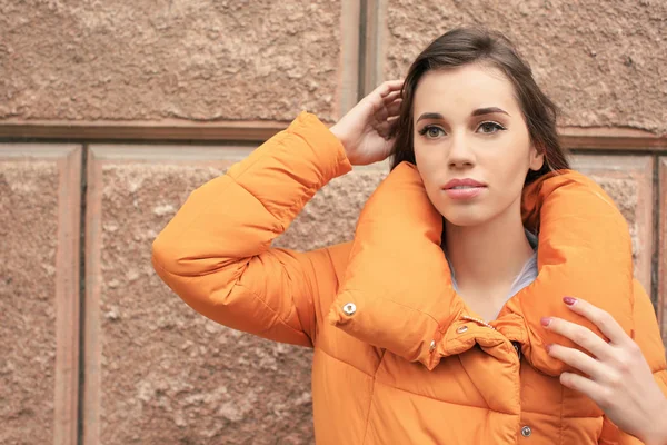 Atractiva mujer sonriente en chaqueta hinchable naranja contra la pared de ladrillo —  Fotos de Stock