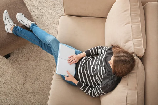 Bella donna che legge libro mentre riposa sul divano a casa — Foto Stock