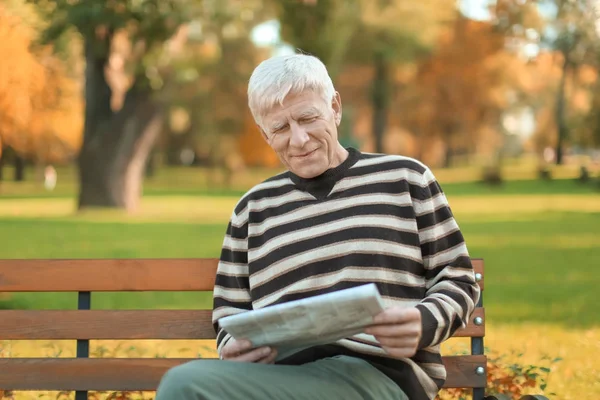 Стильный зрелый мужчина, сидящий на скамейке и читающий газету в осеннем парке — стоковое фото