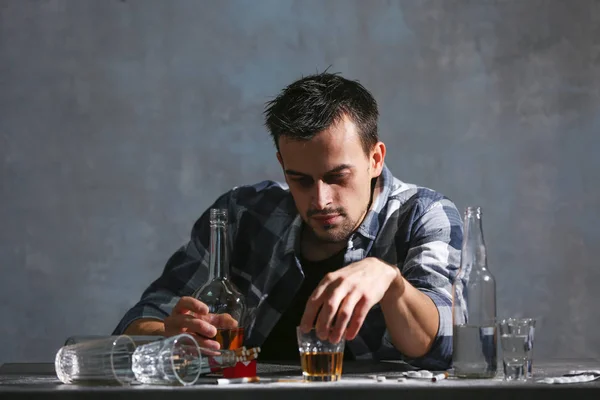 アルコールや薬物とのテーブルに座って酔った男 アルコール依存症の概念 — ストック写真