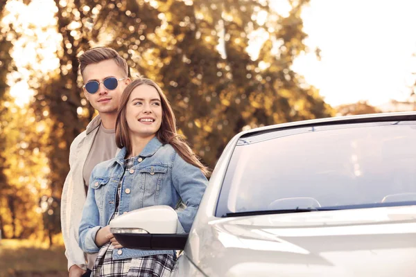 Feliz jovem casal de pé perto de carro moderno ao ar livre — Fotografia de Stock