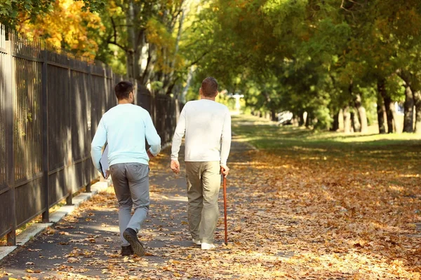 Молодой сиделка гуляет со старшим мужчиной в парке — стоковое фото