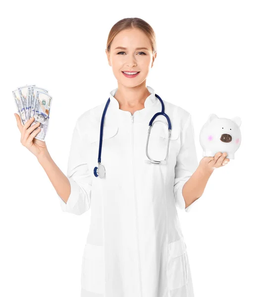 Jovem médico segurando dinheiro e porquinho banco no fundo branco — Fotografia de Stock