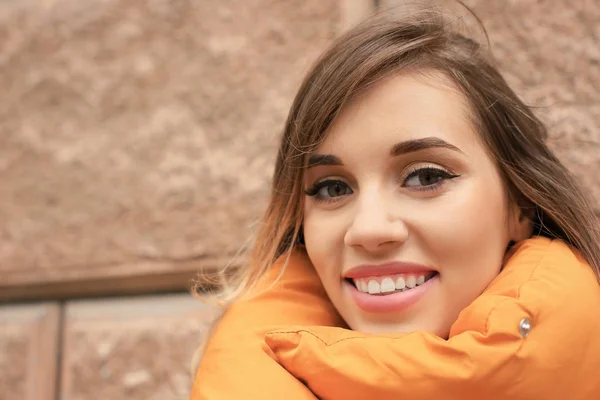 Mulher sorridente atraente em casaco de puffer laranja contra parede de tijolo — Fotografia de Stock