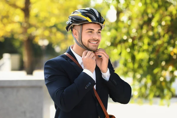 Joven hombre de negocios guapo poniéndose el casco de bicicleta al aire libre — Foto de Stock