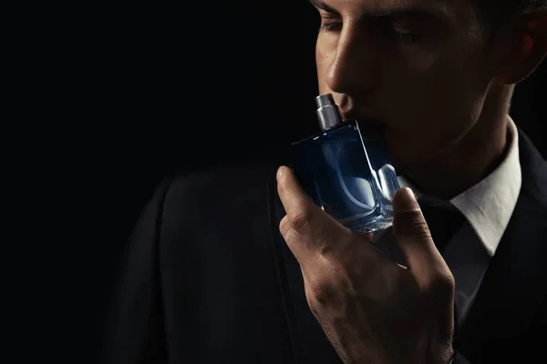 Hombre guapo con botella de perfume sobre fondo oscuro, primer plano —  Fotos de Stock