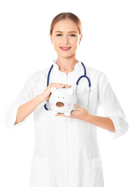 Молодая женщина-врач держит копилку на белом фоне — стоковое фото