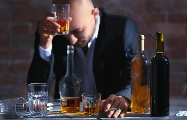 Man drinking whiskey and smoking cigarette at table. Alcoholism concept