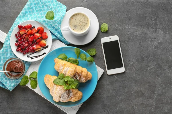 Composizione con gustosi croissant, caffè e telefono cellulare sul tavolo — Foto Stock