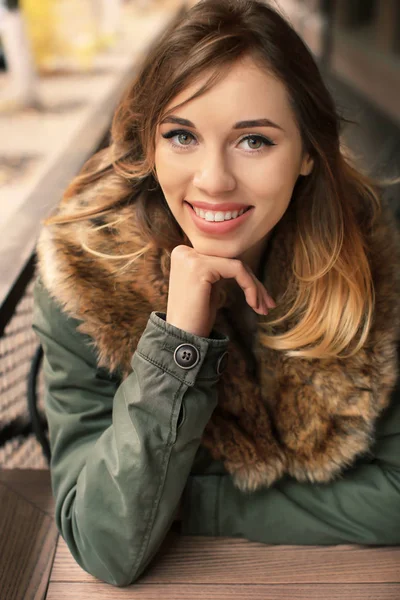 Atractiva mujer sonriente en chaqueta con cuello de piel en la cafetería al aire libre —  Fotos de Stock