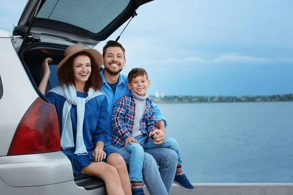 Ung familj med pojken som sitter i bilen stammen nära floden — Stockfoto