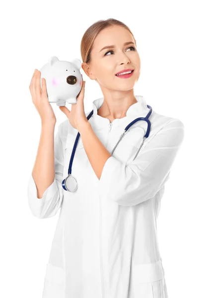 Young female doctor shaking piggy bank on white background — Stock Photo, Image