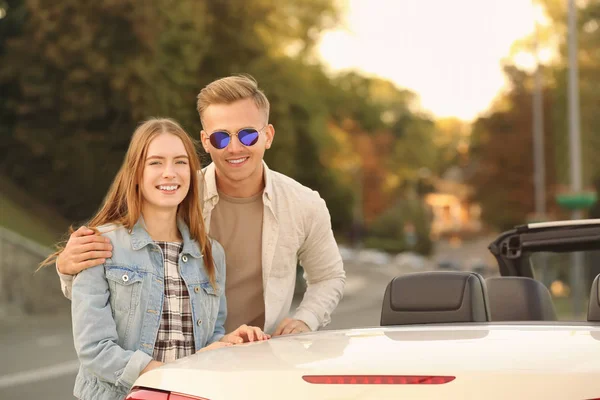 Счастливая молодая пара стоит рядом с современным автомобилем на открытом воздухе — стоковое фото