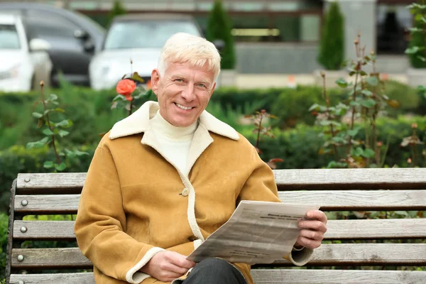 Handsome mature man reading newspaper on bench outdoors — Stock Photo, Image