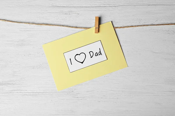 Karte mit dem Satz "i love dad" zum Vatertag auf Schnur vor Holzgrund — Stockfoto