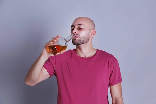 Мужчина пьет виски на сером фоне. Концепция алкоголизма — стоковое фото