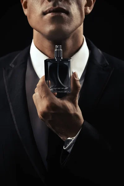 Bello uomo con bottiglia di profumo su sfondo scuro, primo piano — Foto Stock