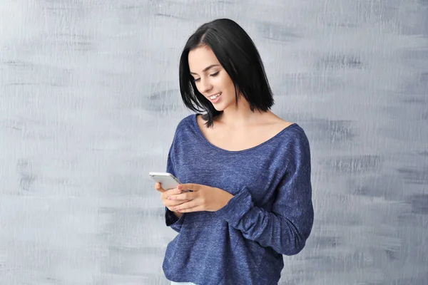 Vacker ung kvinna med mobiltelefon på grå bakgrund — Stockfoto