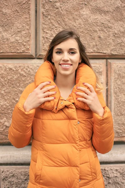 Atrakcyjna kobieta uśmiechający się w pomarańczowy puffer kurtki przeciw mur z cegły — Zdjęcie stockowe
