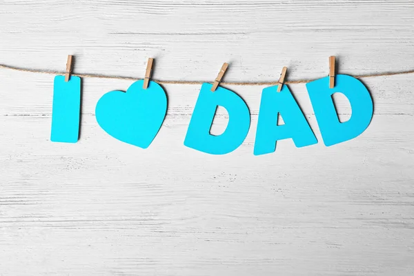 Sanonta "rakastan isää" on tehty paperikirjeistä, joissa tervehditään isänpäivää merkkijonolla puista taustaa vasten. — kuvapankkivalokuva