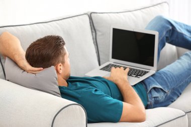 Evde koltukta istirahat ederken dizüstü bilgisayar kullanan yakışıklı adam