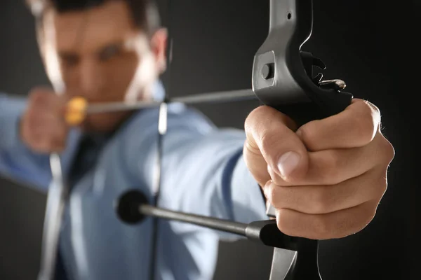 Молодой бизнесмен практикует стрельбу из лука на тёмном фоне — стоковое фото