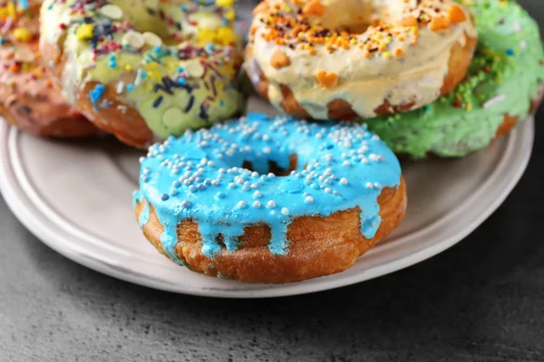 Prato com deliciosos donuts coloridos no fundo cinza — Fotografia de Stock