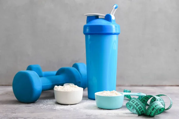 Proteinshake i flaska, pulver, mäta tejp och hantlar på bord — Stockfoto