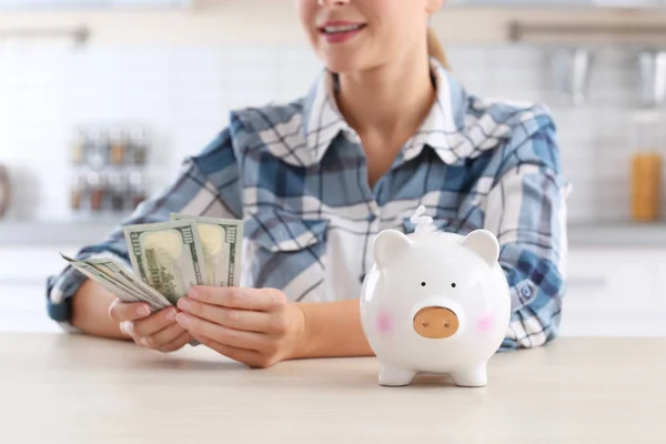 Vrouw met spaarvarken en geld aan tafel, close-up — Stockfoto
