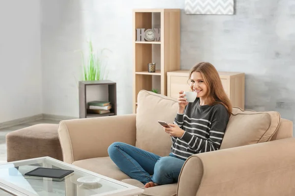 Красива жінка п'є каву, відпочиваючи на дивані вдома — стокове фото