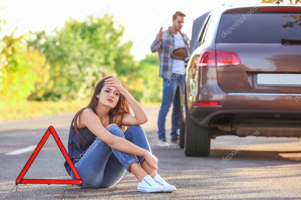 Young woman and man with broken car on background