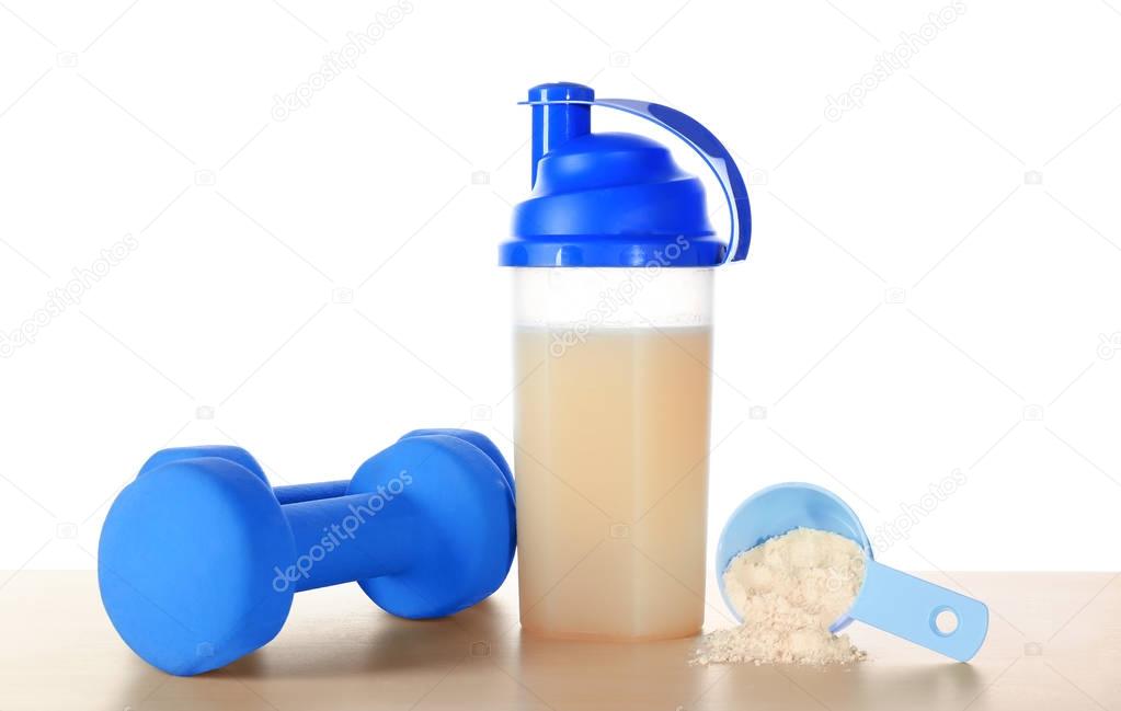 Protein shake in bottle, scoop with powder and dumbbells on table