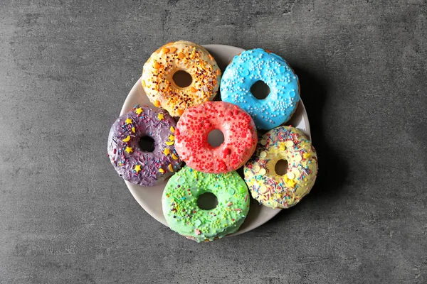 Placa con deliciosas rosquillas de colores sobre fondo gris — Foto de Stock